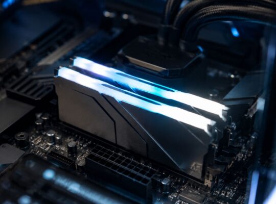 Two DDR5 RAM sticks installed in a gaming motherboard inside a PC case with blue RGB lighting and visible motherboard components in the background