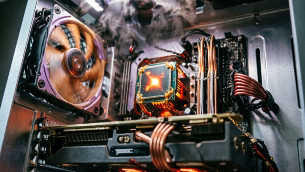 Close-up of an open PC case showing a spinning case fan, a glowing hot CPU cooler area, visible heat and smoke-like vapor, and a graphics card in the foreground.